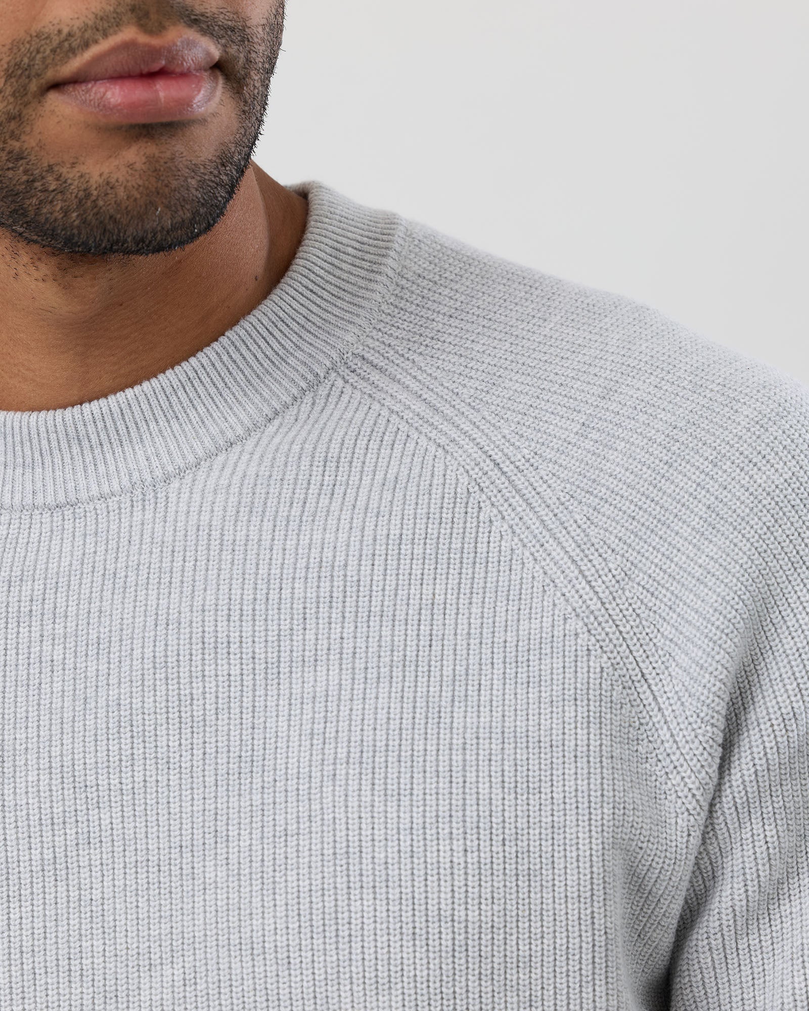 Close-up of a person wearing a light grey sweater against a neutral background