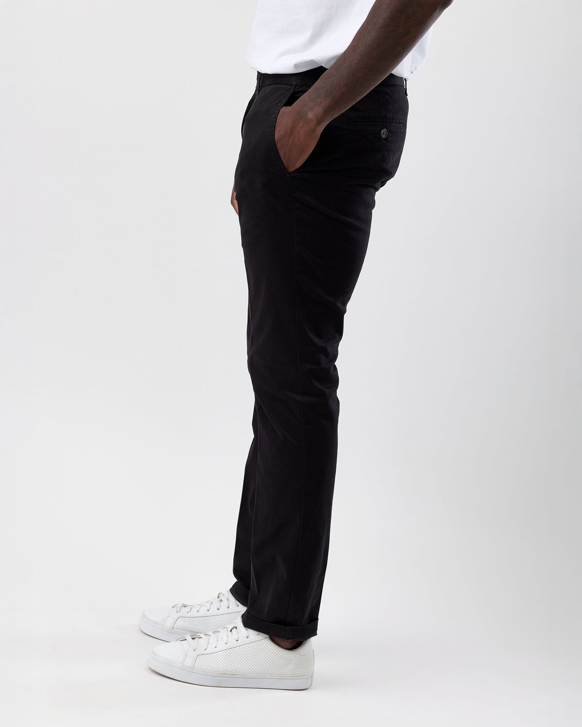 Person wearing Wayver black chinos and white sneakers on a white background, side view