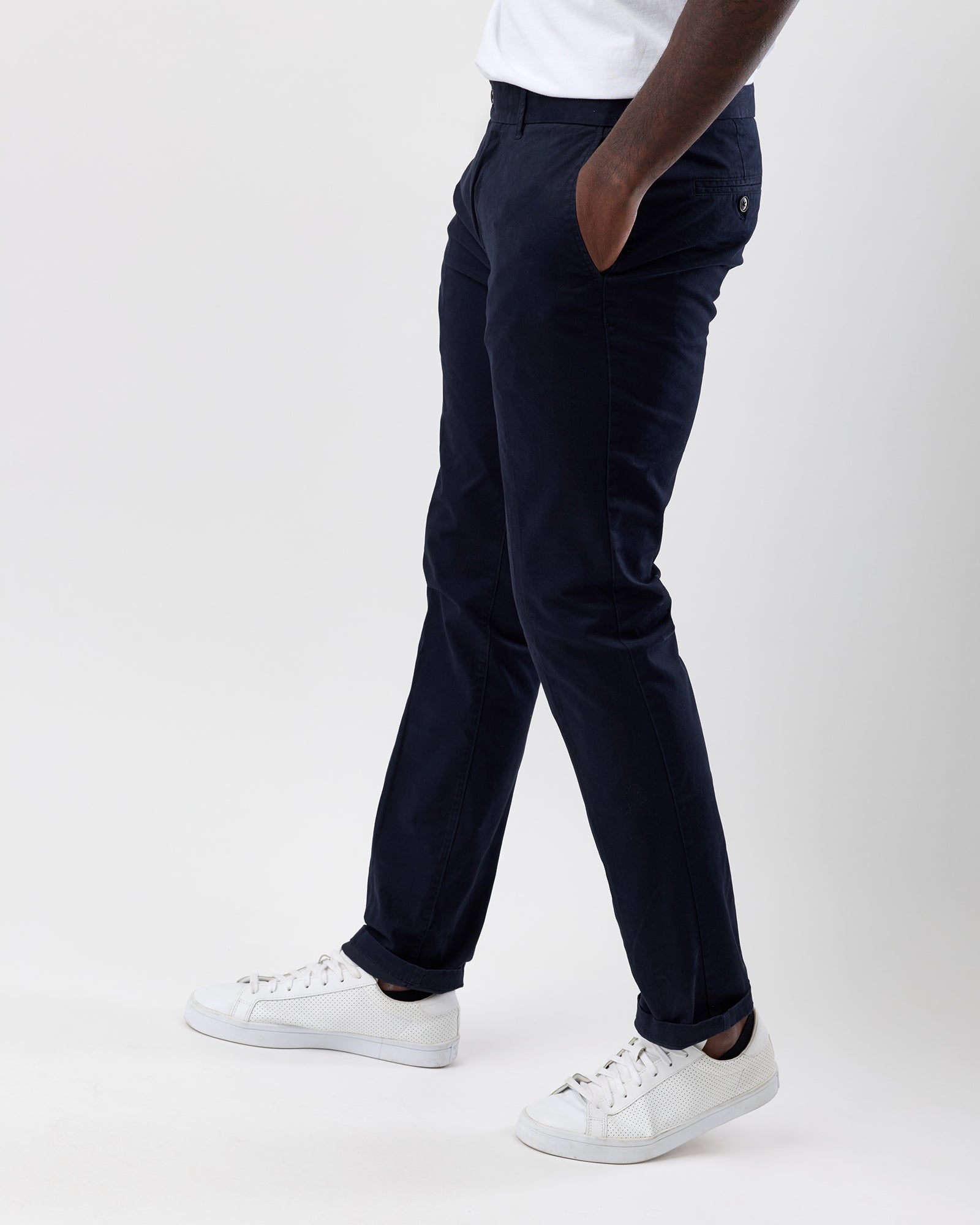 Person wearing navy straight leg pants and white sneakers on a white background