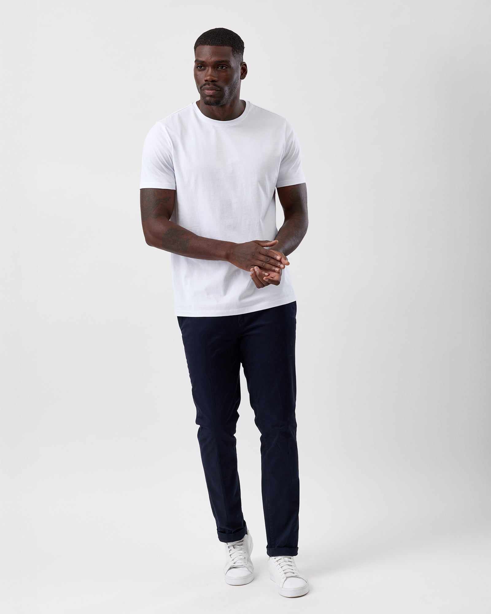 Man wearing a white t-shirt, navy cotton stretch chino pants, and white sneakers on a plain background, street styled, full body shot