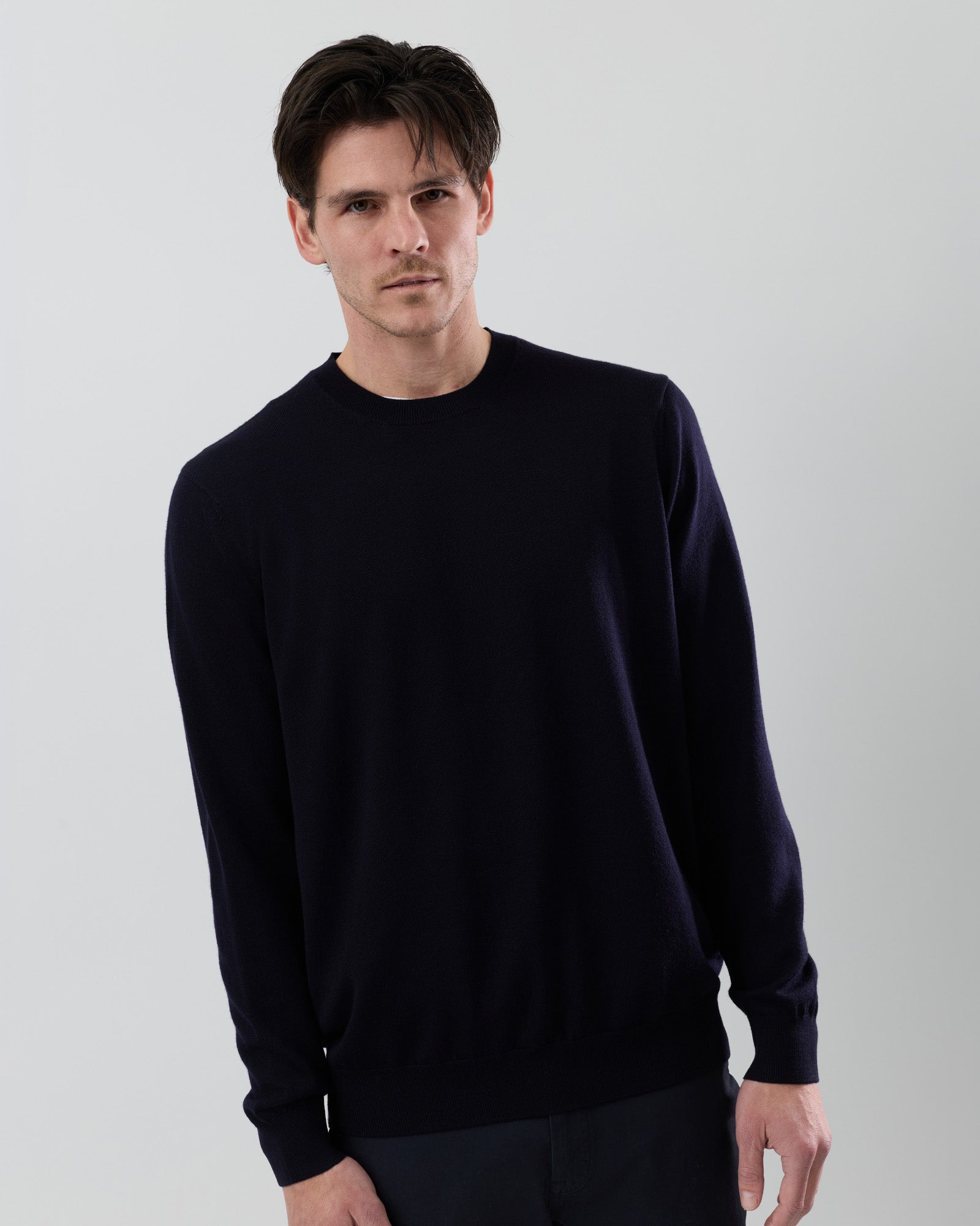 Side angle of a men's navy Australian ultrafine merino crew neck sweater, highlighting the tailored fit and premium knit fabric against a grey background.