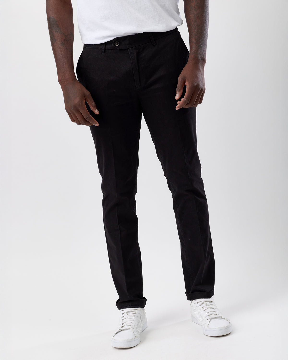 Person wearing black straight leg pants and white sneakers on a white background