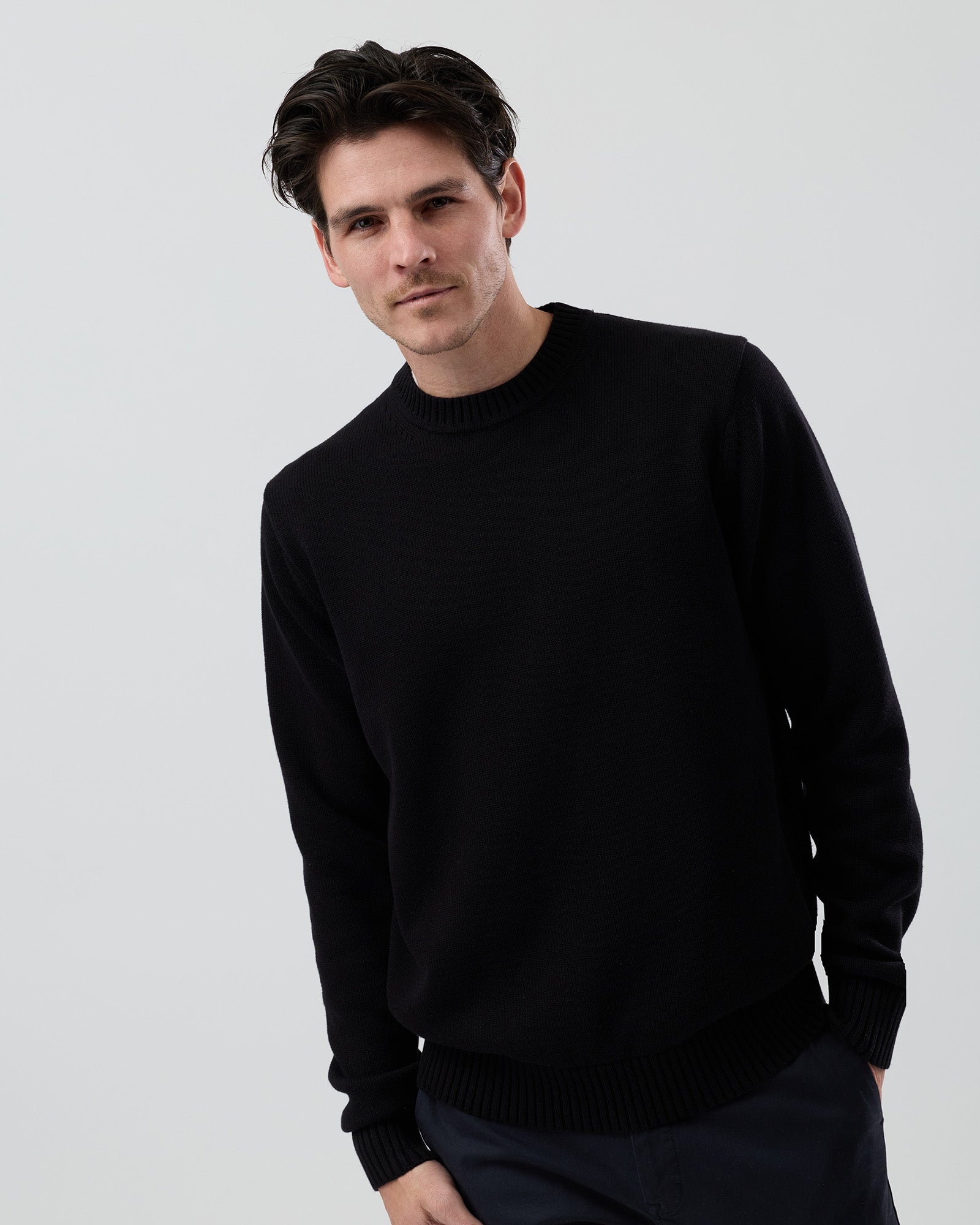 Male model wearing the Wayver Essential Cotton Crew Neck Knit in black, front cropped view showing the regular fit and slim sleeve profile on a grey background.