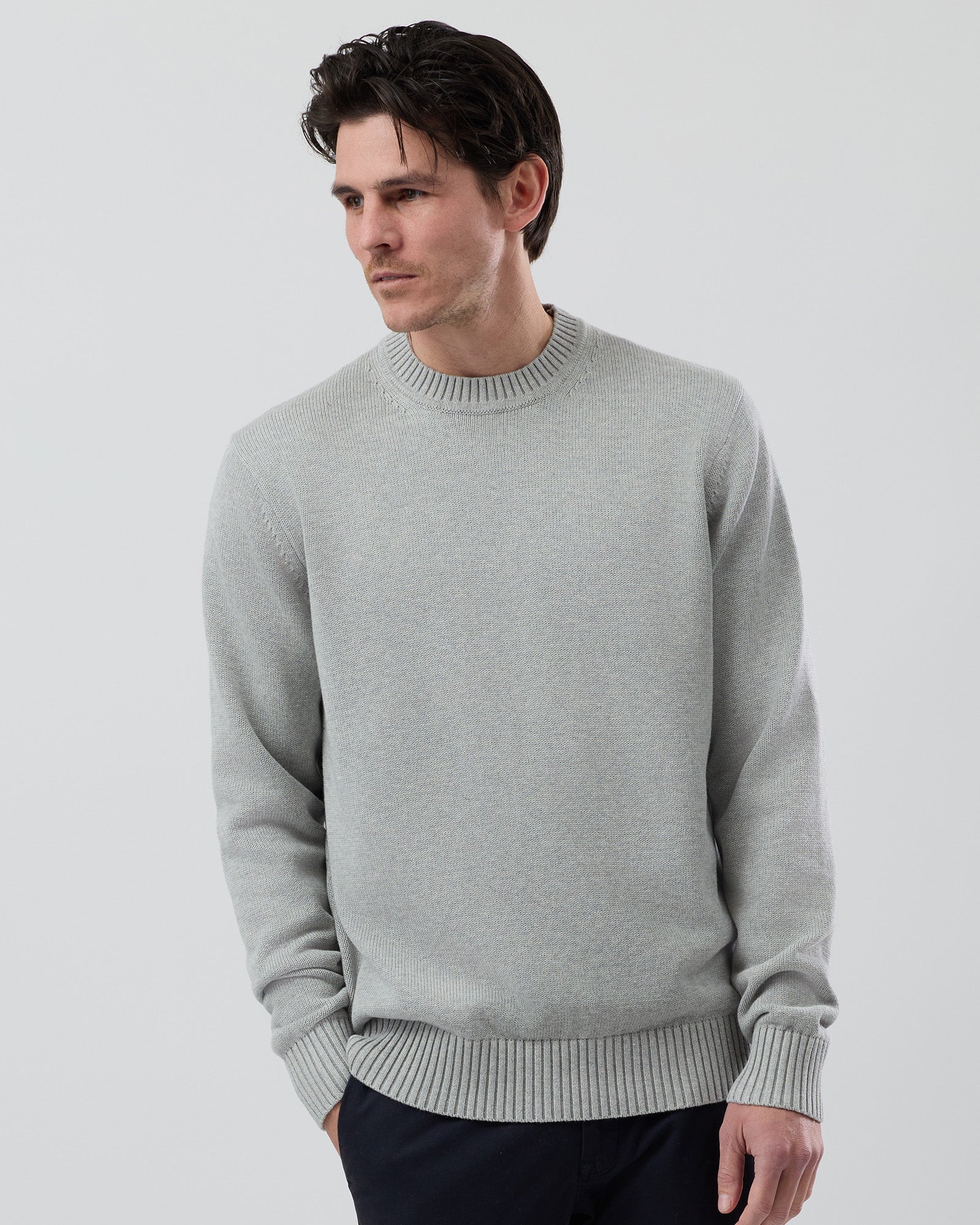Side profile of a male model wearing the Wayver light grey cotton crew neck jumper with navy chinos showing the comfortable everyday fit.