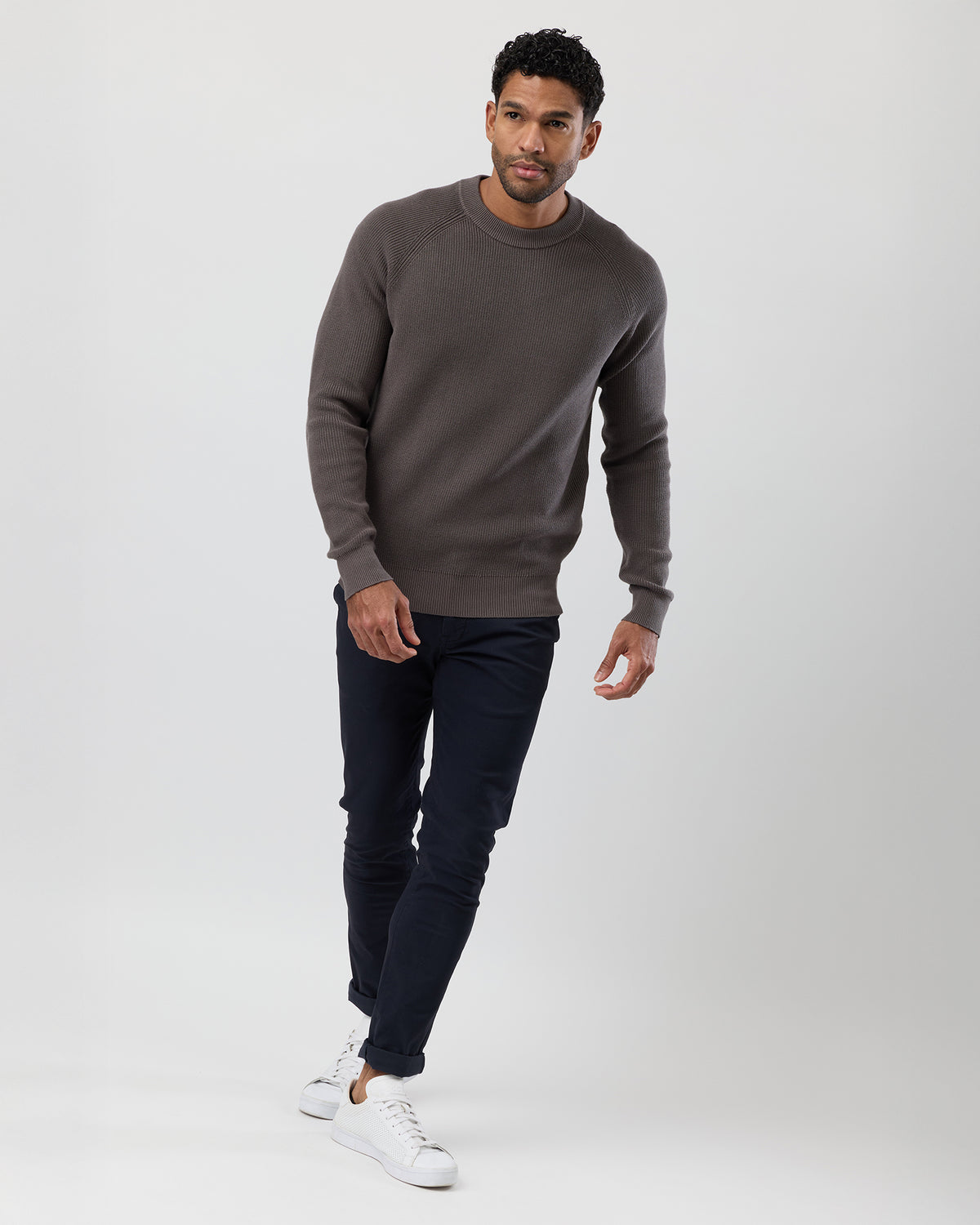 Man wearing a brown sweater and dark pants and white sneakers on a white background, full body image