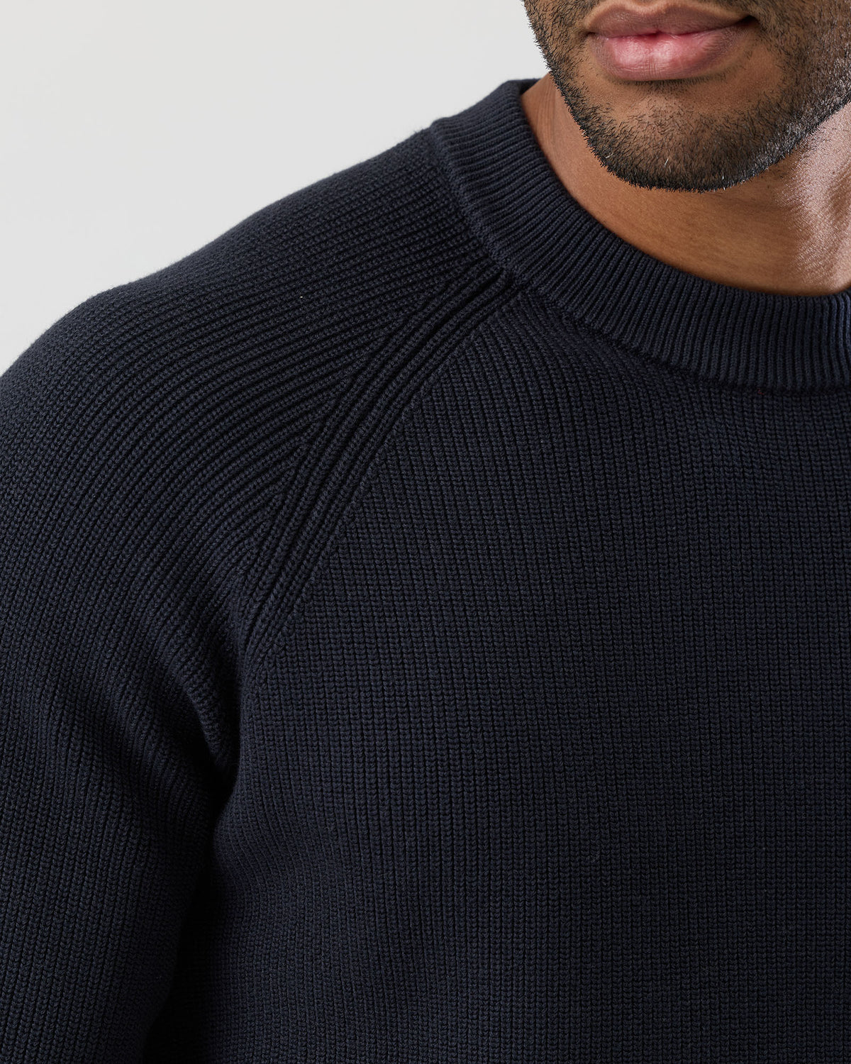 Close-up of a person wearing a black sweater against a light gray background