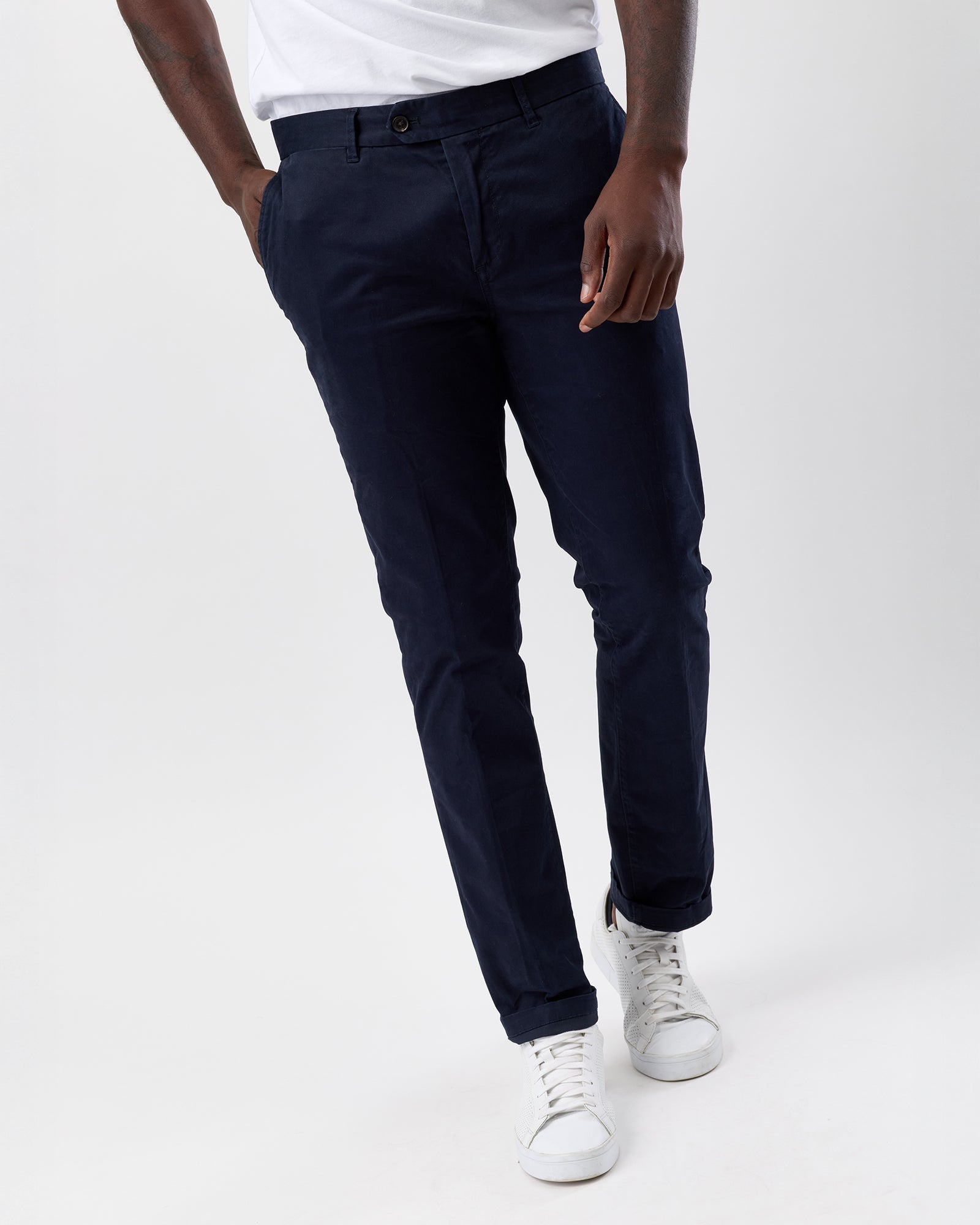 Person wearing navy straight leg pants and white sneakers on a white background