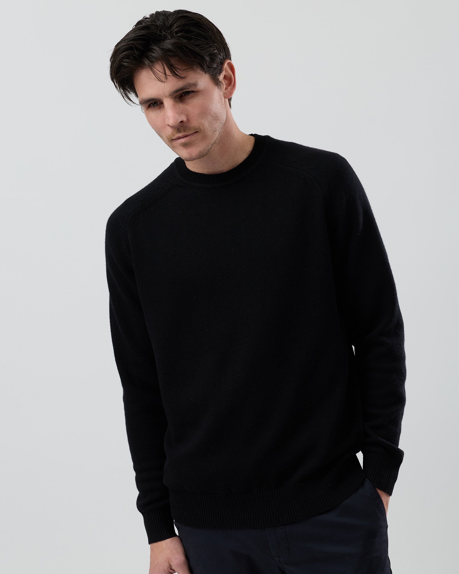 Male model wearing the Wayver Originals black wool blend crew neck knit on a grey background, front cropped view highlighting the fit through the chest and sleeves.