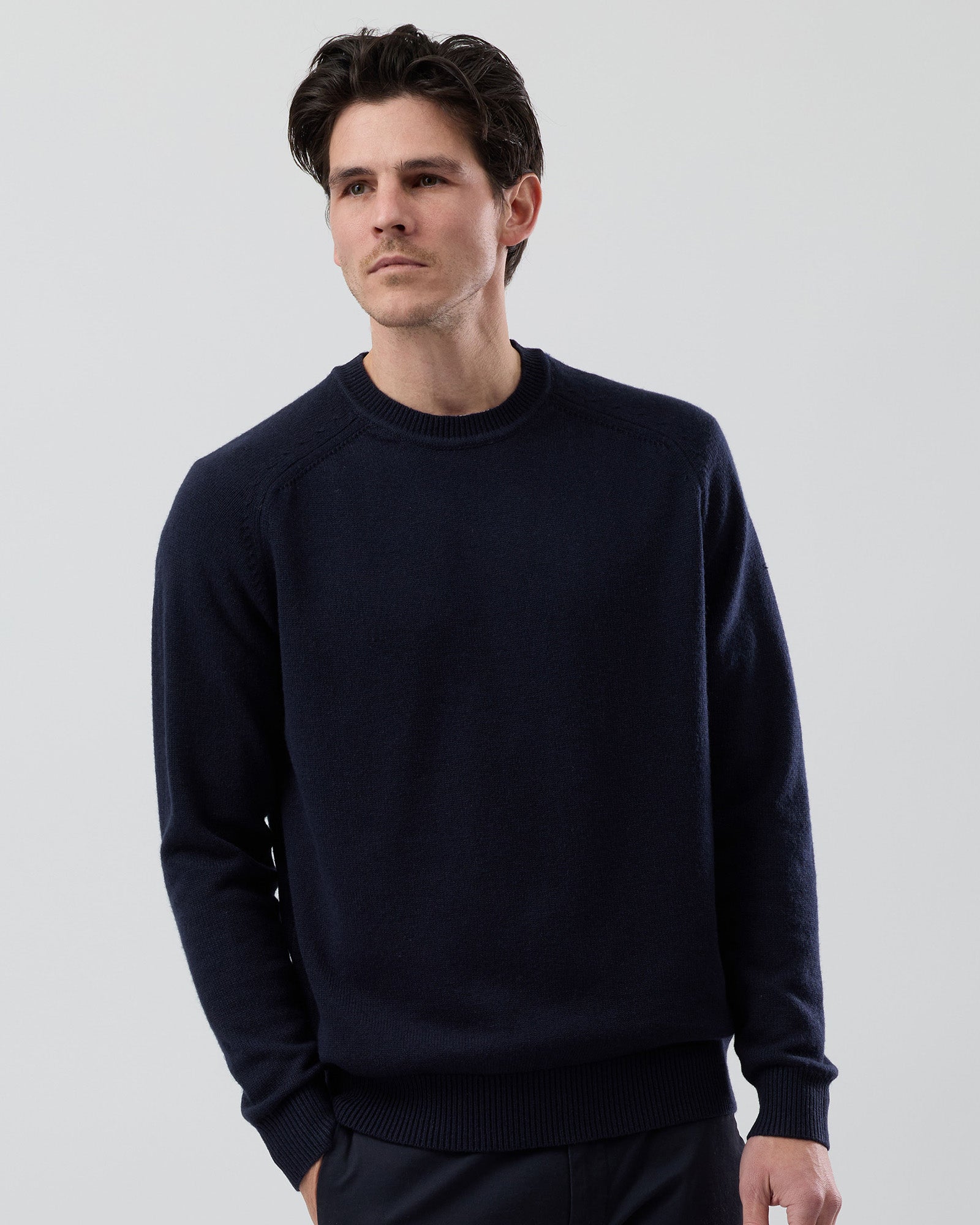 Male model wearing the Wayver Originals navy wool blend crew neck knit on a grey background, front cropped view highlighting the fit through the chest and sleeves.
