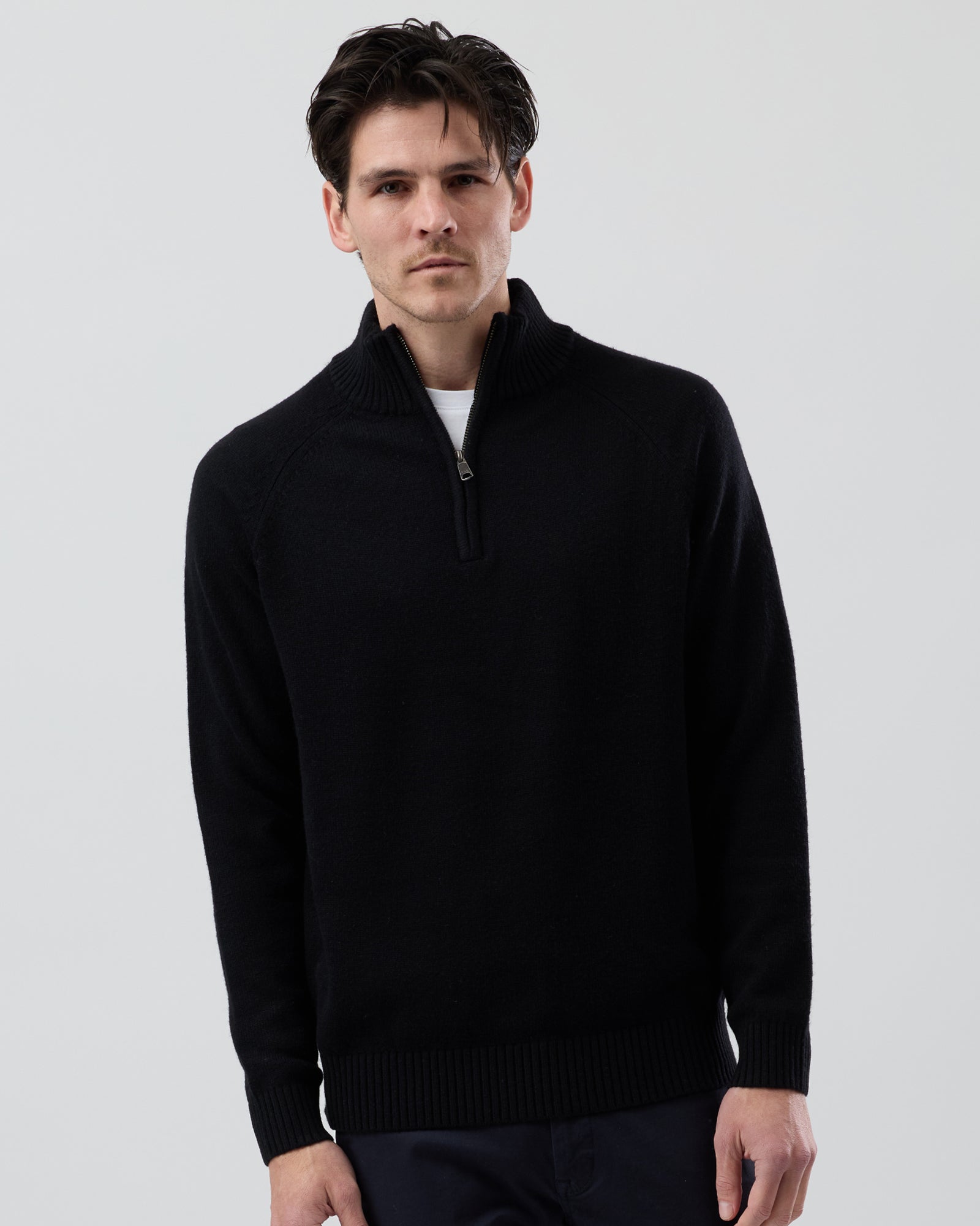 Male model wearing the Wayver black wool blend half zip knit, front view showing the stand collar, regular fit and slim sleeve design on a grey background.