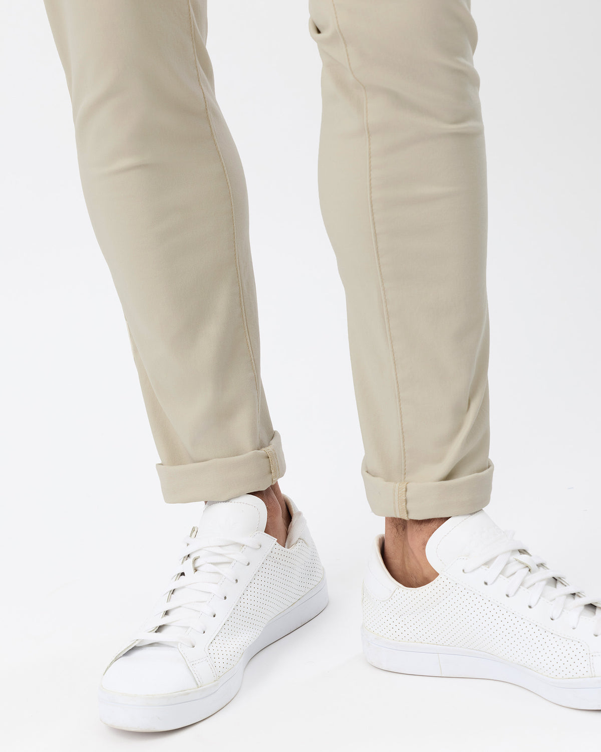 Close-up of men's beige slim stretch chinos showing the tapered lower legs, rolled cuffs and white sneakers.