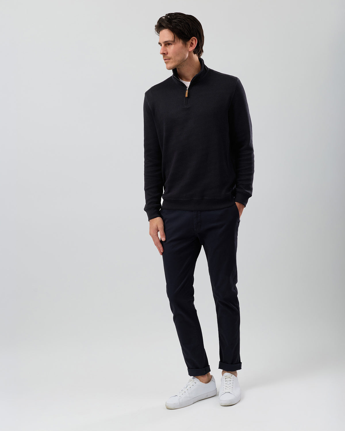 Model wearing a black quarter zip sweater with navy chinos, featuring a textured French rib cotton knit, long sleeves and ribbed hem.